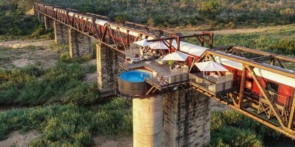 Aerial view of luxury Shalati train lodge on a bridge with a pool and deck in KNP, South Africa.