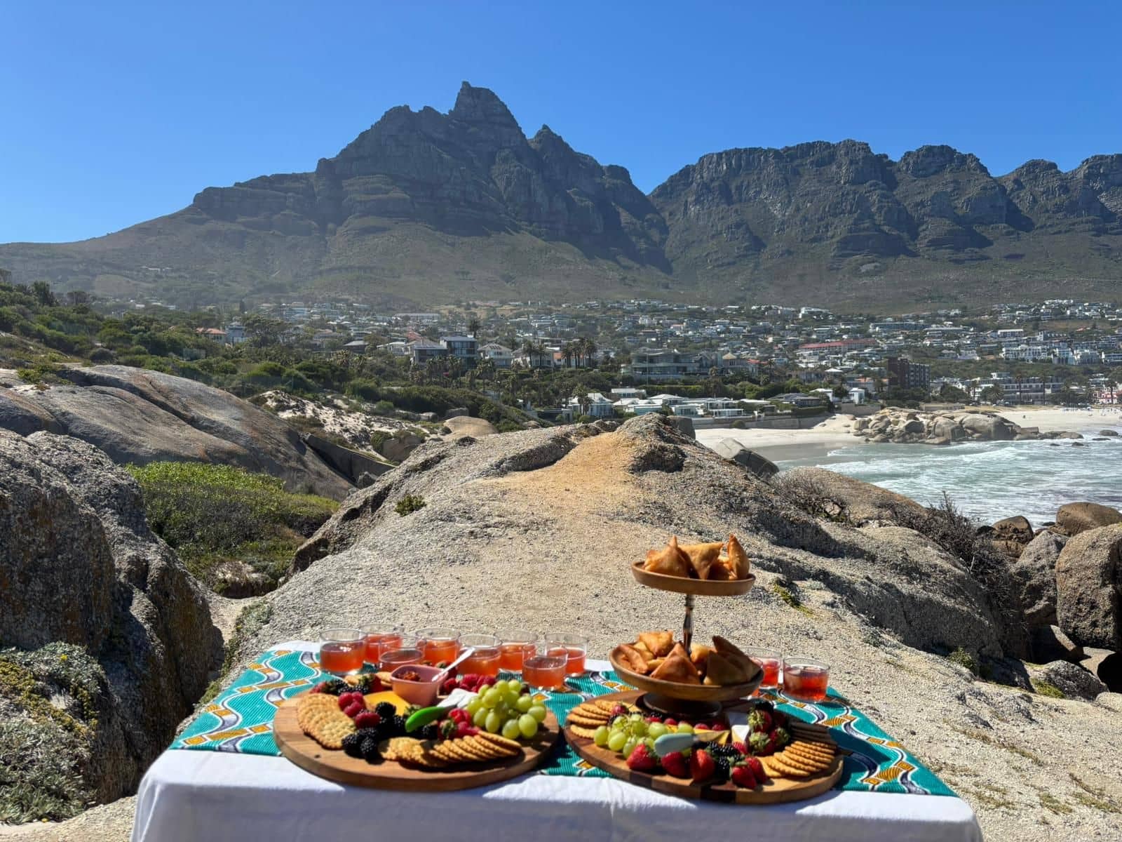 Cape Town picnic spread with fruit and pastries set against the Twelve Apostles mountain range above Camps Bay, South Africa.