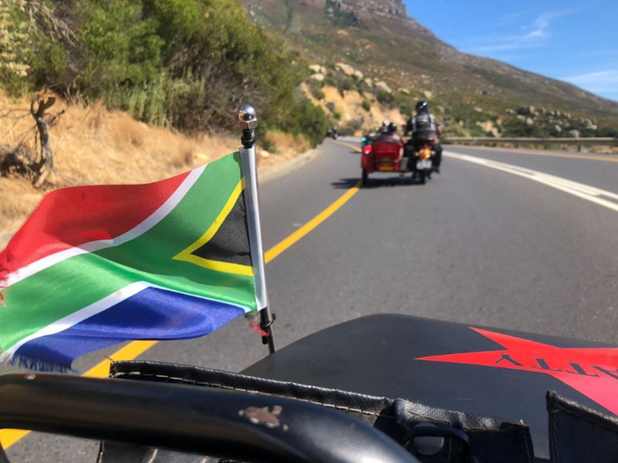 View from a vintage sidecar with a South African flag, following other sidecars along a mountain road near Cape Town.